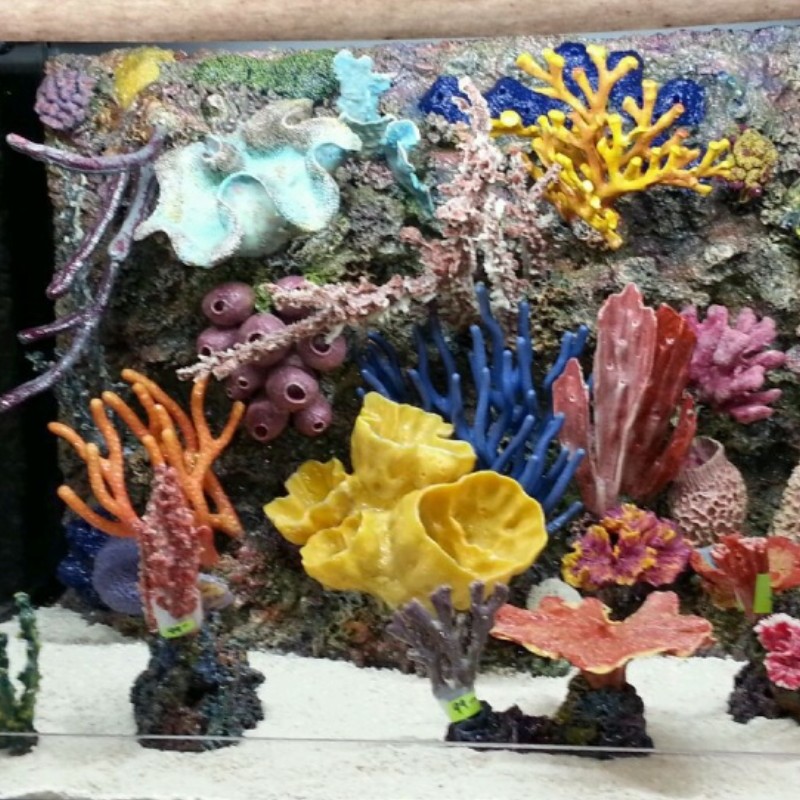 A wall of colorful artificial coral pieces in yellow, blue, red and orange inside an aquarium.