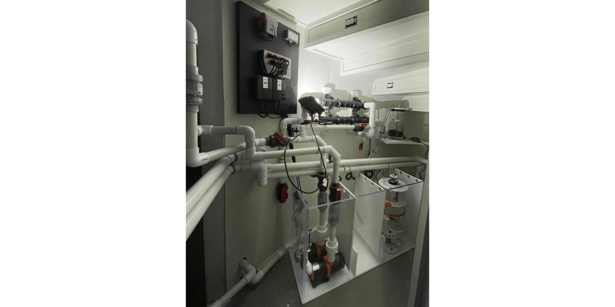A black-and-white photo of white plumbing, pumps and a control panel inside an aquarium equipment cabinet.