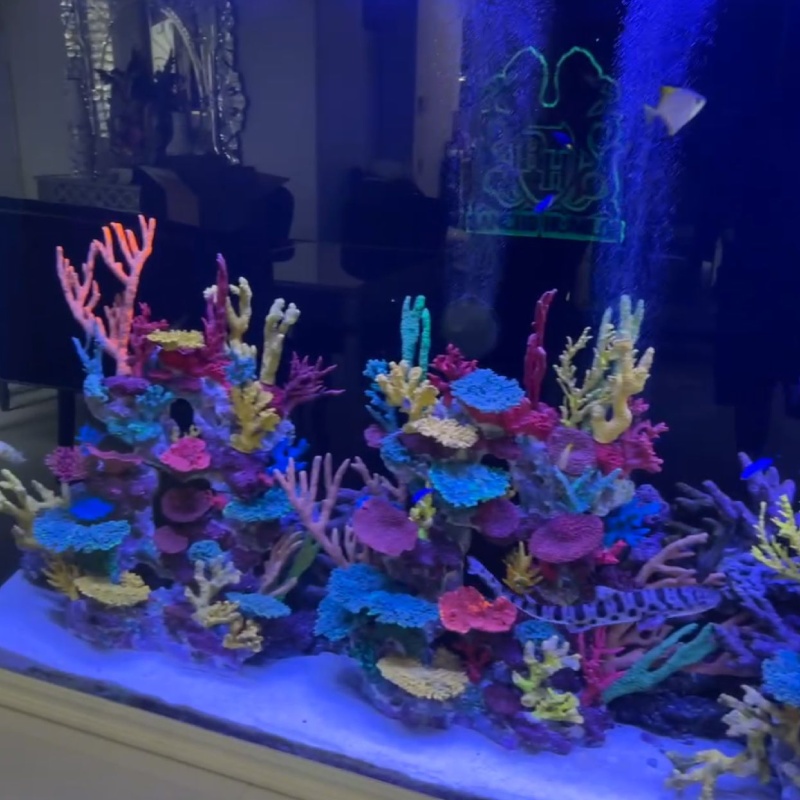 An aquarium aquascaped with brightly colored artificial coral under blue light.