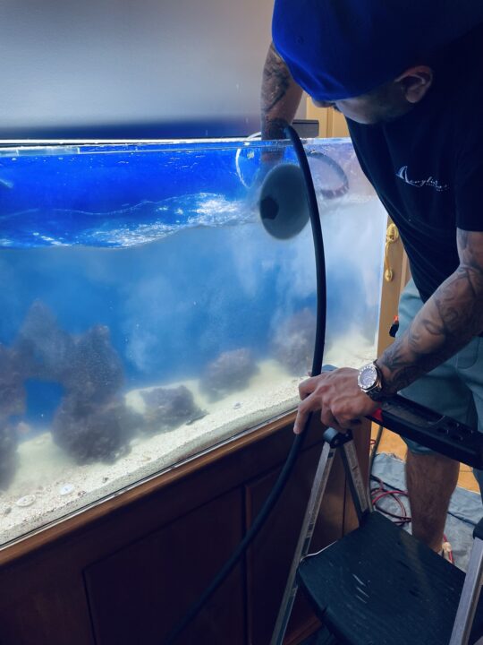 A technician polishing the front panel of an aquarium filled with water and rockwork.